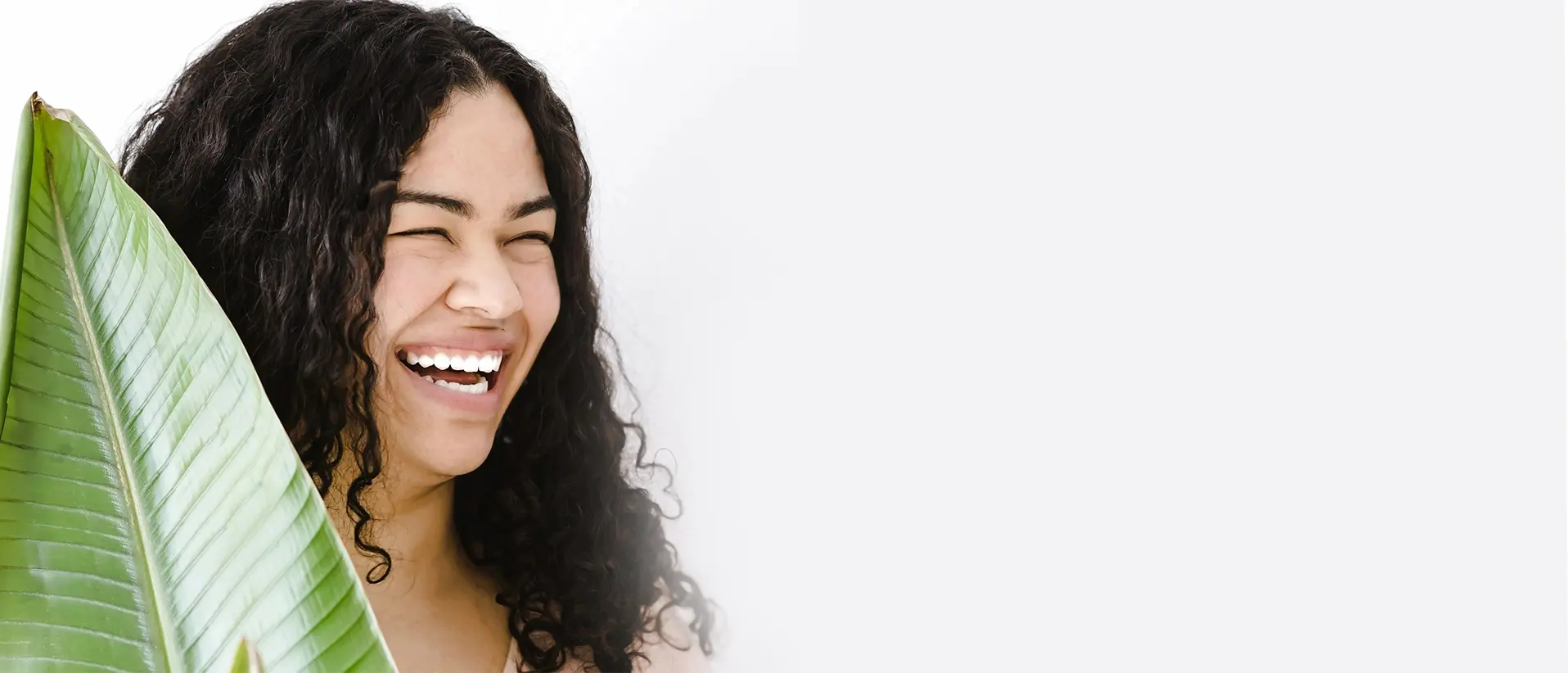 Woman with curly hair laughing near green leaf.