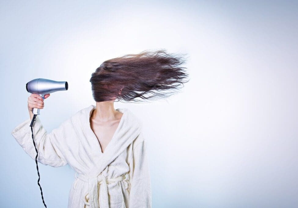 Woman in robe drying hair with hairdryer.